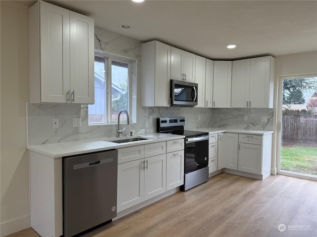 kitchen featuring light hardwood / wood-style floors, appliances with stainless steel finishes, decorative backsplash, white cabinets, and sink