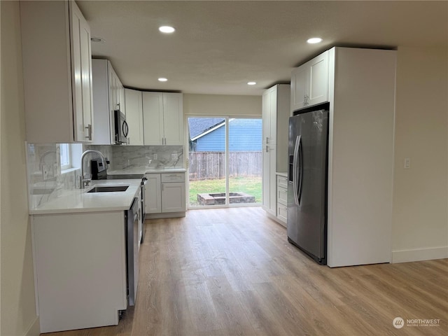 kitchen featuring light hardwood / wood-style floors, appliances with stainless steel finishes, tasteful backsplash, white cabinets, and sink