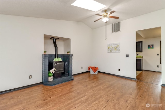 living room featuring ceiling fan, hardwood / wood-style floors, a wood stove, and lofted ceiling with skylight