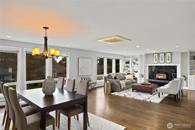 dining room with built in shelves, recessed lighting, an inviting chandelier, a premium fireplace, and wood finished floors