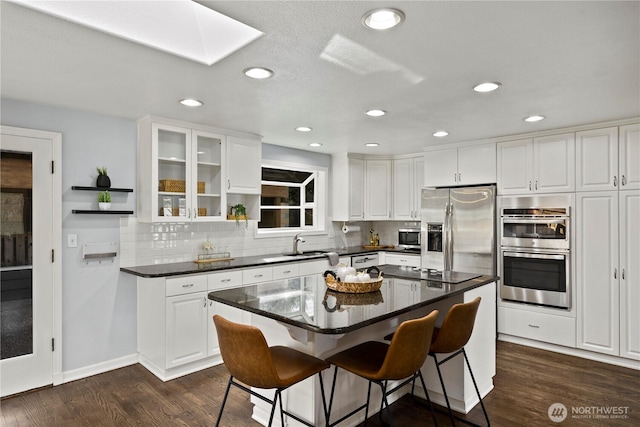 kitchen featuring appliances with stainless steel finishes, dark countertops, dark wood-style flooring, and a skylight