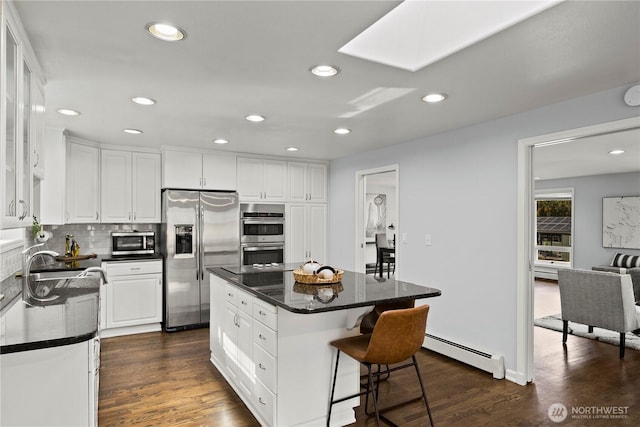 kitchen with stainless steel appliances, a baseboard heating unit, white cabinetry, a sink, and a kitchen breakfast bar