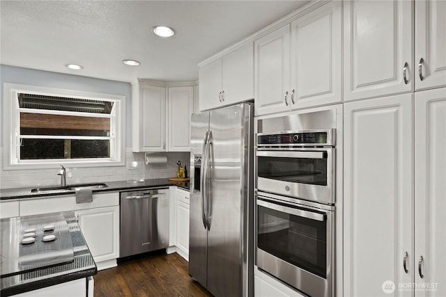 kitchen featuring dark countertops, appliances with stainless steel finishes, white cabinets, and a sink