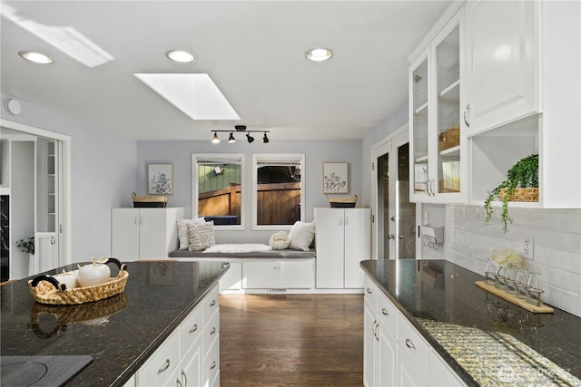 kitchen featuring recessed lighting, dark wood-type flooring, a skylight, decorative backsplash, and glass insert cabinets