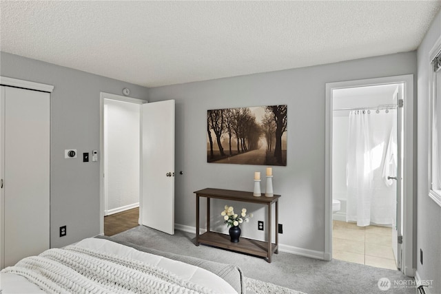 carpeted bedroom featuring ensuite bathroom, a textured ceiling, a closet, and baseboards