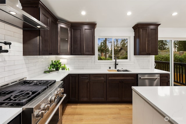 kitchen featuring wall chimney exhaust hood, stainless steel appliances, light hardwood / wood-style floors, sink, and backsplash