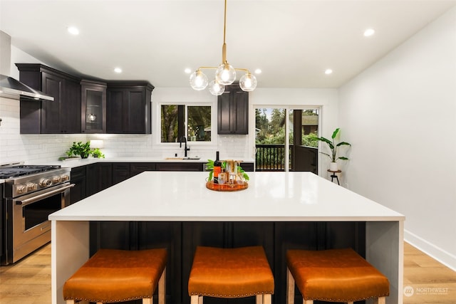 kitchen featuring a kitchen island, sink, stainless steel range with gas cooktop, a kitchen breakfast bar, and wall chimney exhaust hood