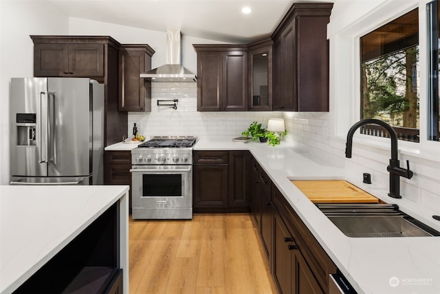 kitchen featuring lofted ceiling, wall chimney range hood, tasteful backsplash, sink, and high quality appliances