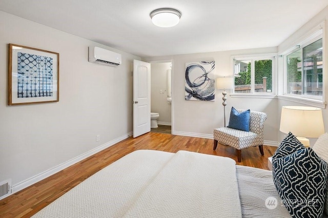 bedroom featuring light hardwood / wood-style floors, connected bathroom, and a wall mounted air conditioner