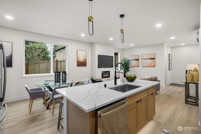 kitchen with appliances with stainless steel finishes, a kitchen island with sink, light stone countertops, pendant lighting, and sink