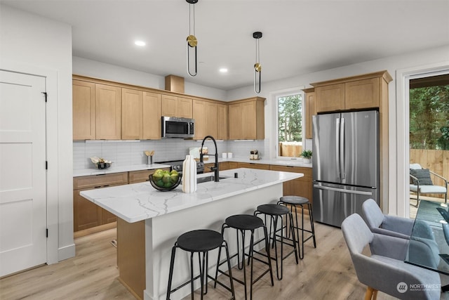 kitchen with appliances with stainless steel finishes, decorative light fixtures, light hardwood / wood-style floors, sink, and a center island with sink