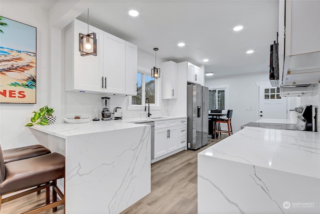 kitchen with decorative light fixtures, white cabinets, appliances with stainless steel finishes, and light stone countertops