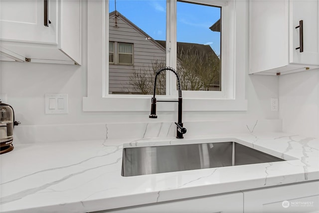 interior details featuring sink, light stone counters, and white cabinetry