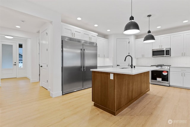 kitchen featuring sink, a kitchen island with sink, white cabinetry, hanging light fixtures, and stainless steel appliances