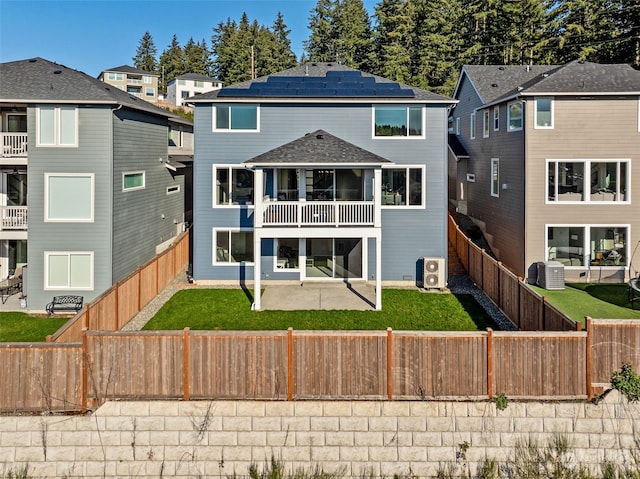 rear view of house with central AC, solar panels, a lawn, a balcony, and a patio area