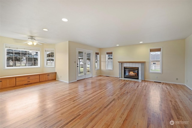 unfurnished living room featuring a healthy amount of sunlight, light hardwood / wood-style floors, and a tiled fireplace