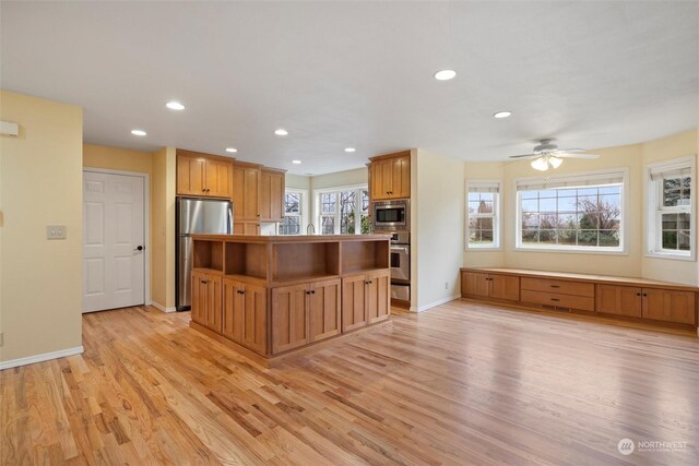 kitchen with ceiling fan, stainless steel appliances, a kitchen island, and light wood-type flooring