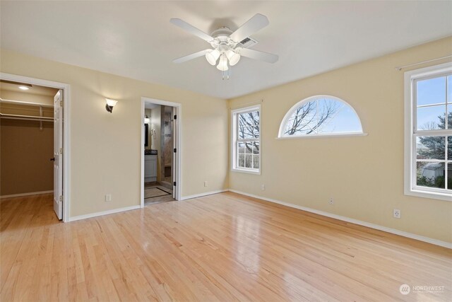 unfurnished bedroom with ceiling fan, light wood-type flooring, ensuite bath, a walk in closet, and a closet