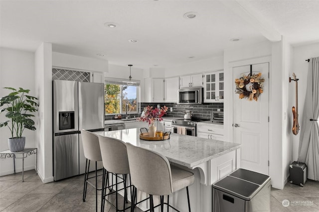 kitchen with pendant lighting, a kitchen island, sink, stainless steel appliances, and white cabinets