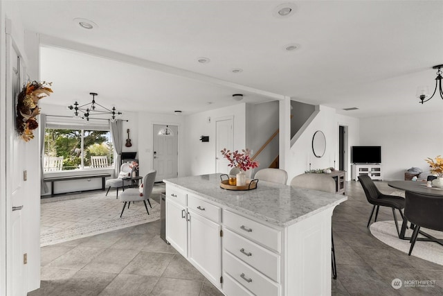 kitchen featuring light stone countertops, a kitchen island, white cabinetry, a notable chandelier, and a breakfast bar