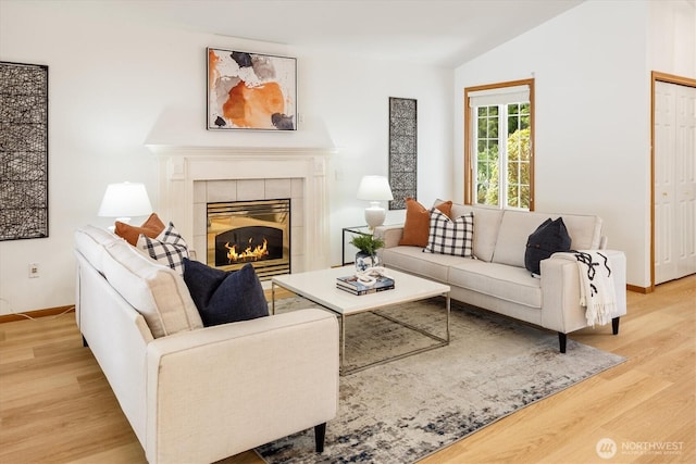 living room with lofted ceiling, light wood finished floors, baseboards, and a tiled fireplace