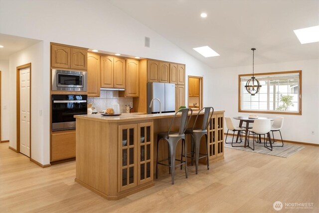 kitchen with a center island with sink, glass insert cabinets, appliances with stainless steel finishes, light countertops, and pendant lighting