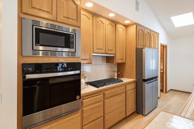 kitchen featuring light wood finished floors, stainless steel appliances, light countertops, backsplash, and lofted ceiling with skylight