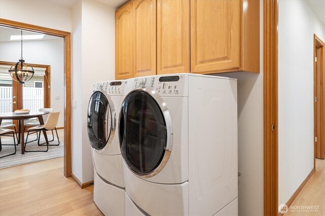 washroom featuring cabinet space, baseboards, light wood-style floors, washing machine and dryer, and a chandelier