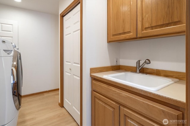 washroom with light wood finished floors, cabinet space, washing machine and dryer, a sink, and baseboards