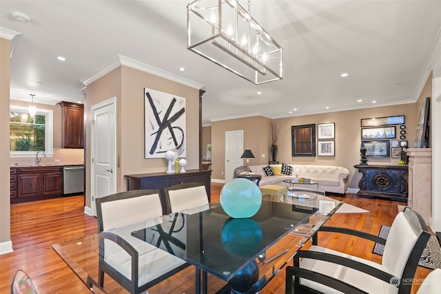 dining area featuring a notable chandelier, light hardwood / wood-style flooring, sink, and crown molding