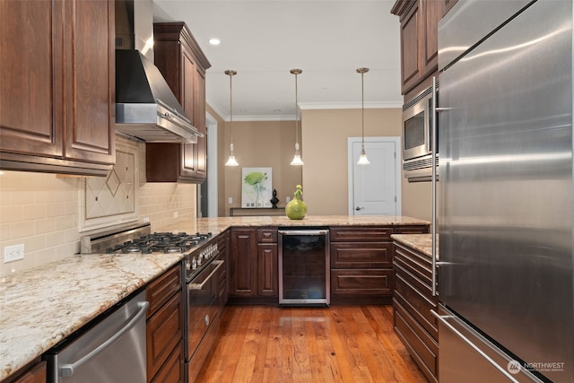 kitchen with built in appliances, wall chimney range hood, decorative light fixtures, crown molding, and beverage cooler