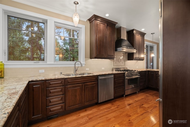 kitchen featuring sink, wall chimney range hood, stainless steel appliances, and decorative light fixtures