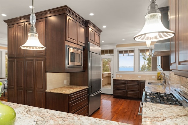 kitchen with decorative light fixtures, built in appliances, sink, light stone counters, and dark hardwood / wood-style floors