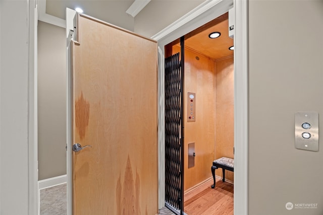 corridor with ornamental molding, wood-type flooring, and elevator