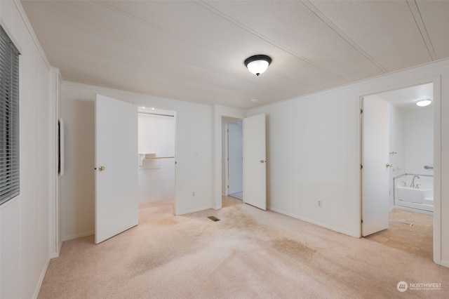 unfurnished bedroom featuring light colored carpet, connected bathroom, a closet, and crown molding