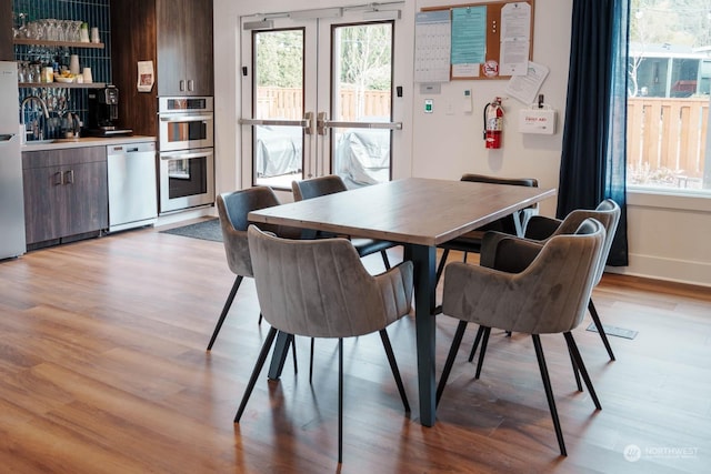 dining area with sink, french doors, and light wood-type flooring