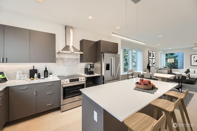 kitchen featuring wall chimney exhaust hood, a breakfast bar area, tasteful backsplash, hanging light fixtures, and appliances with stainless steel finishes