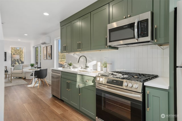 kitchen with backsplash, a wall unit AC, green cabinets, light hardwood / wood-style flooring, and appliances with stainless steel finishes