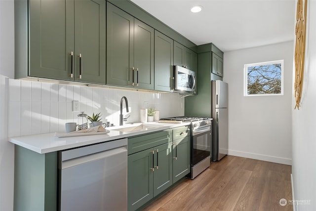 kitchen with appliances with stainless steel finishes, tasteful backsplash, light wood-type flooring, green cabinetry, and sink