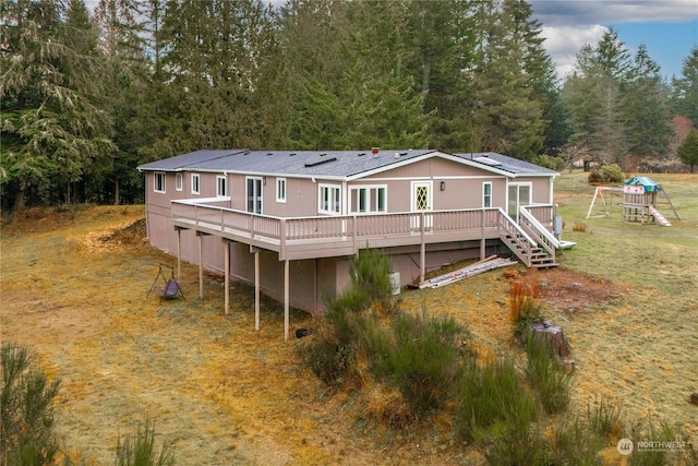 back of house featuring a playground, a deck, and a lawn