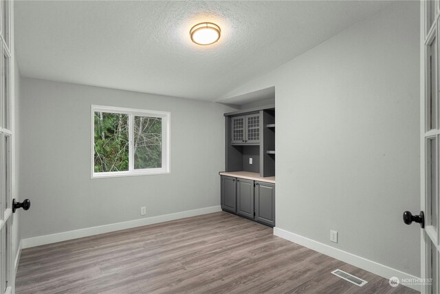 spare room with light wood-type flooring, vaulted ceiling, and a textured ceiling