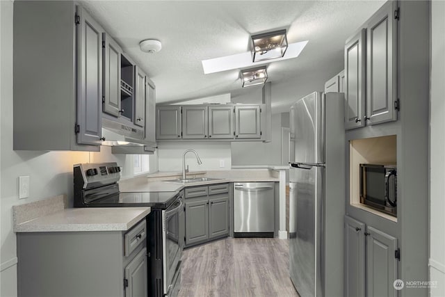 kitchen with gray cabinets, stainless steel appliances, lofted ceiling with skylight, and sink