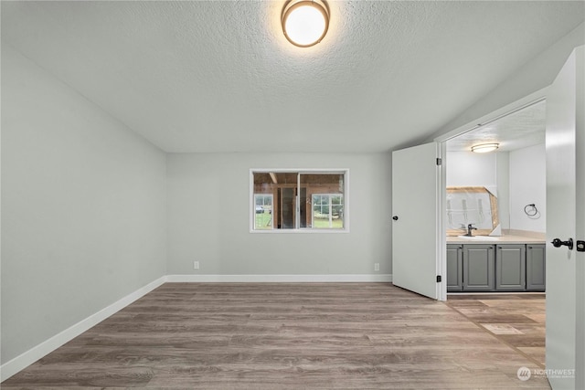 spare room with light wood-type flooring, sink, and a textured ceiling