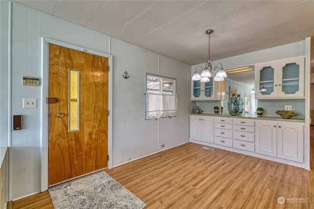 interior space featuring white cabinetry, hanging light fixtures, an inviting chandelier, wooden walls, and light wood-type flooring