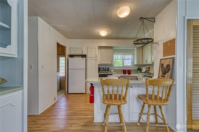 kitchen with white cabinetry, light wood-type flooring, a kitchen breakfast bar, kitchen peninsula, and white fridge