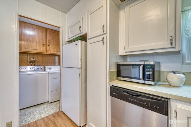 kitchen with stainless steel appliances, white cabinetry, washing machine and clothes dryer, and light hardwood / wood-style flooring