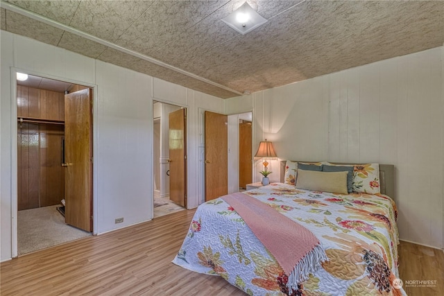 bedroom with connected bathroom, hardwood / wood-style floors, and wood walls