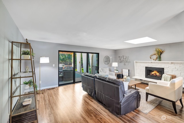 living room with a skylight, light wood-type flooring, and a stone fireplace