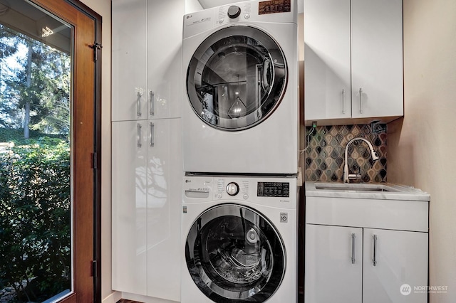 laundry room with sink, stacked washer / dryer, and cabinets