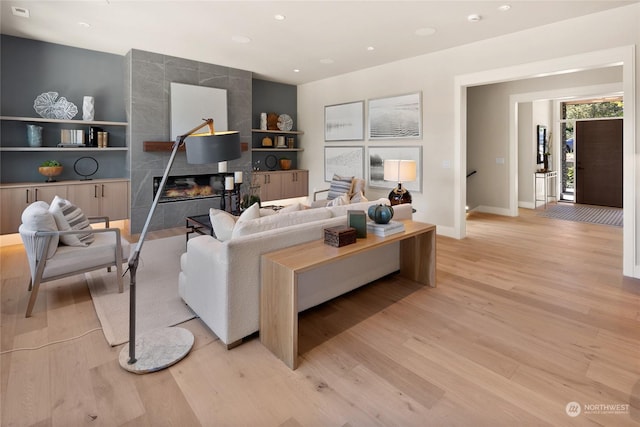 living room with baseboards, a high end fireplace, light wood-type flooring, built in shelves, and recessed lighting